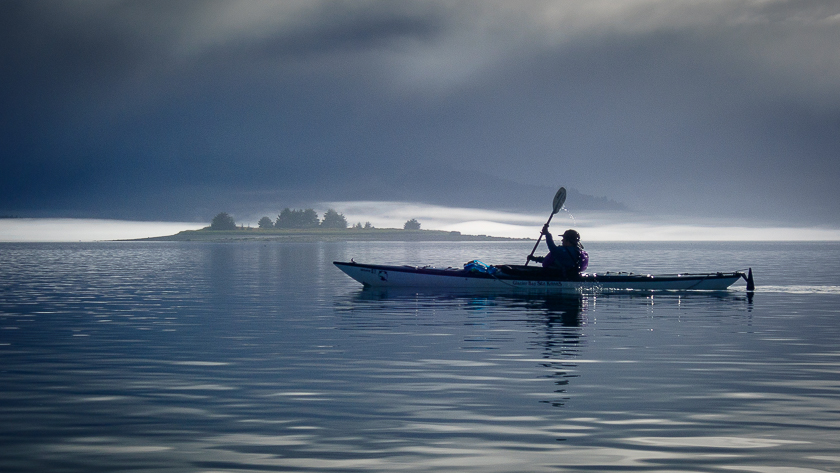 A silhouetted kayaker glides across the calm waters surrounding the Beardslee Islands on a foggy day in Glacier Bay National Park and Preserve. In the background is Eider Island Glacier Bay National Park is located in southeast Alaska. The park is also an important marine wilderness area known for its spectacular tidewater glaciers, icefields, and tall coastal mountains. The park, a popular destination for cruise ships, is also known for its sea kayaking and wildlife viewing opportunities.  Glacier Bay National Park is home to humpback whales which feed in the park's protected waters during the summer, both black and grizzly bears, moose, wolves, sea otters, harbor seals, steller's sea lions, and numerous species of sea birds.  The dynamically changing park, known for its large, contiguous, intact ecosystems, is a United Nations biosphere reserve and a UNESCO World Heritage site.